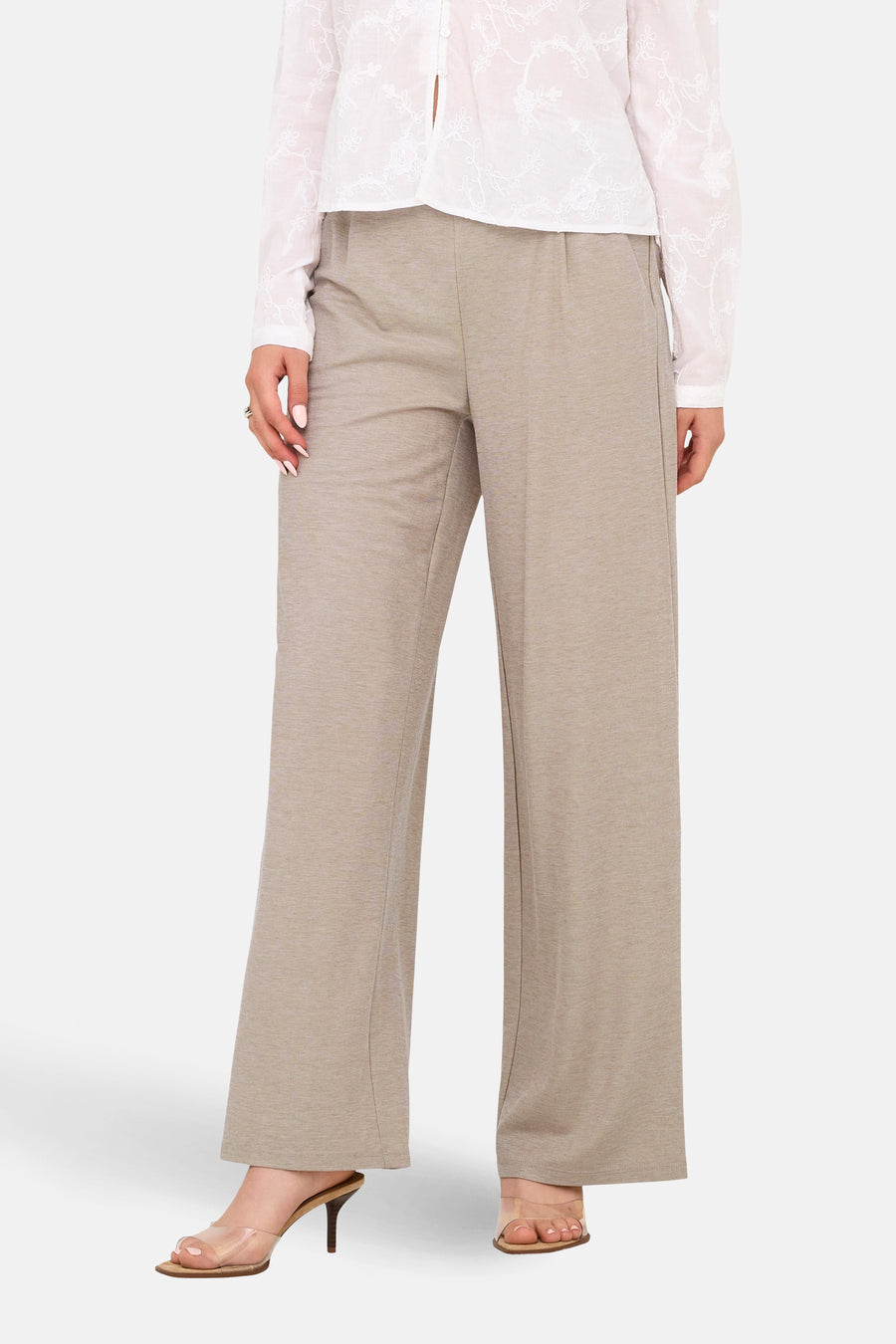 Beige broek van JDY, met wijde pijpen en gedragen met transparante hakken en een witte blouse.