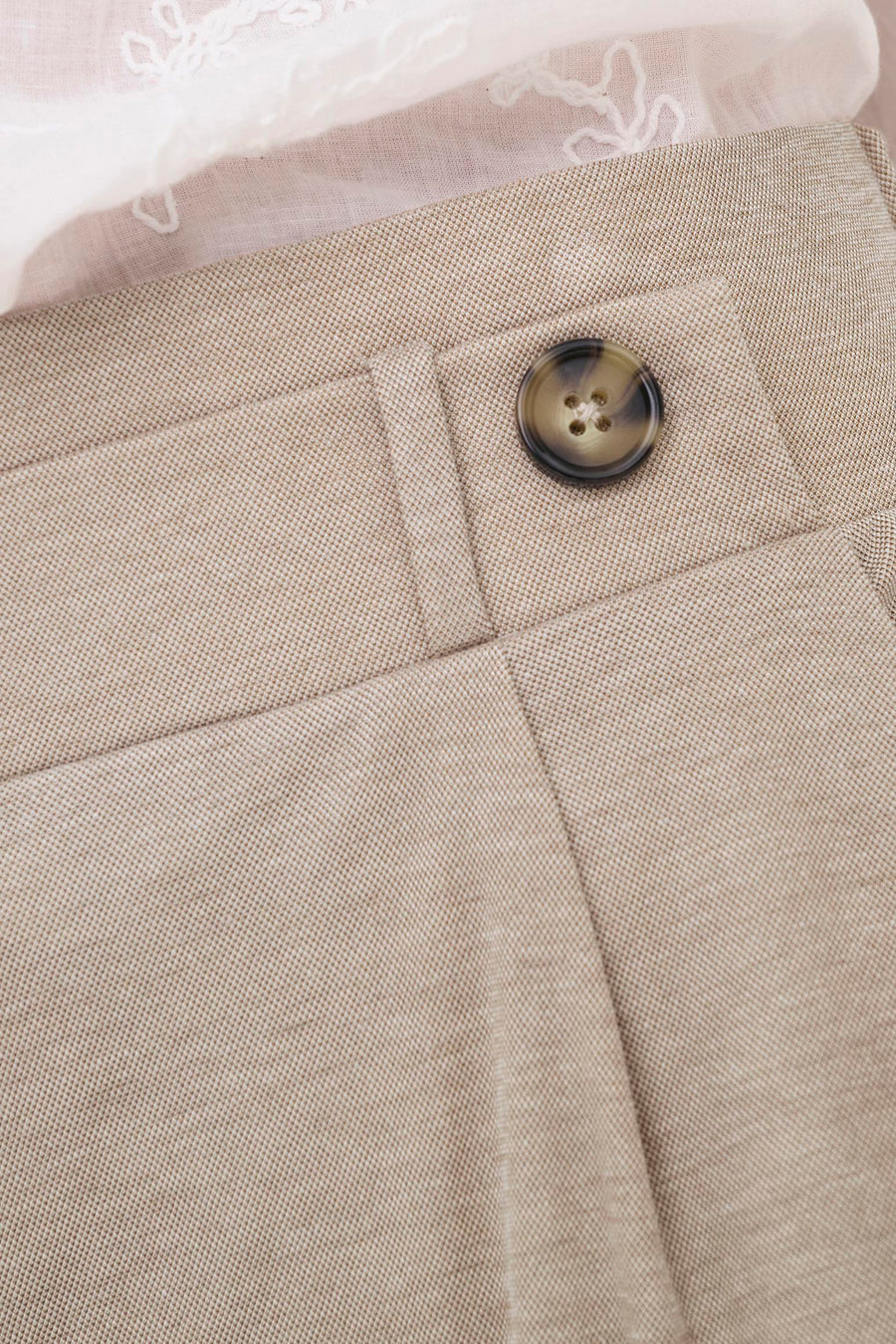 Beige broek van JDY met een bruine knoop, fijne textuur en witte kanten top erboven.