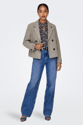 Beige korte jas van ONLY, met een dubbele rij knopen, gedragen met een blouse en blauwe jeans.
