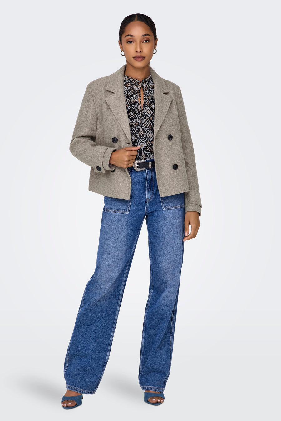 Beige korte jas van ONLY, met dubbele knoopsluiting, gedragen over een bedrukte blouse en wijde jeans.
