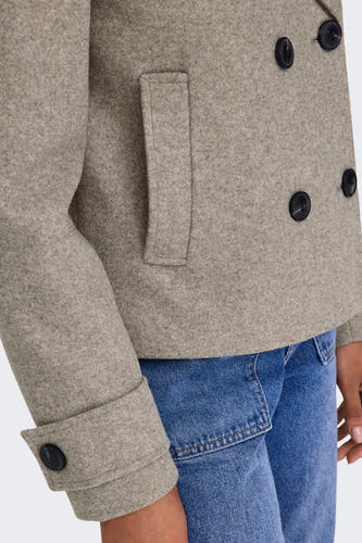 Beige korte jas van ONLY, met donkere knopen en een opgestikte zak, gecombineerd met een blauwe jeans.
