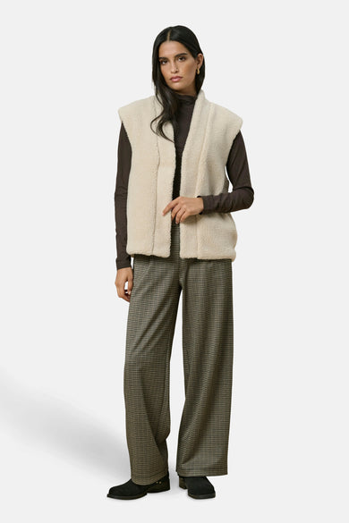 Gilet beige de JDY, porté avec un pull à manches longues marron et un pantalon large à carreaux.