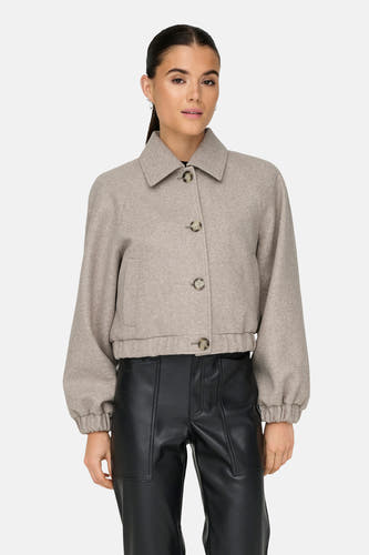 Beige korte jas van ONLY, met kraag en lange pofmouwen, gedragen met een zwarte broek.

