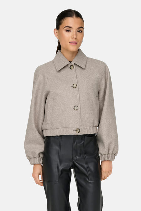 Beige korte jas van ONLY, met kraag en lange pofmouwen, gedragen met een zwarte broek.
