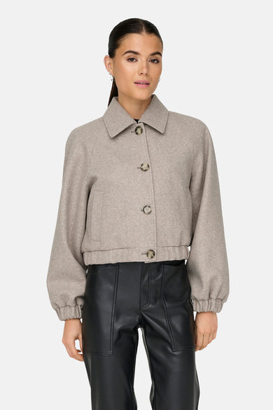 Beige korte jas van ONLY, met kraag en lange pofmouwen, gedragen met een zwarte broek.

