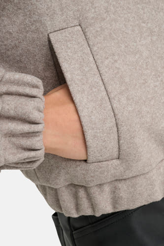 Manteau court beige d'ONLY, avec une main dans la poche et un col élastique.