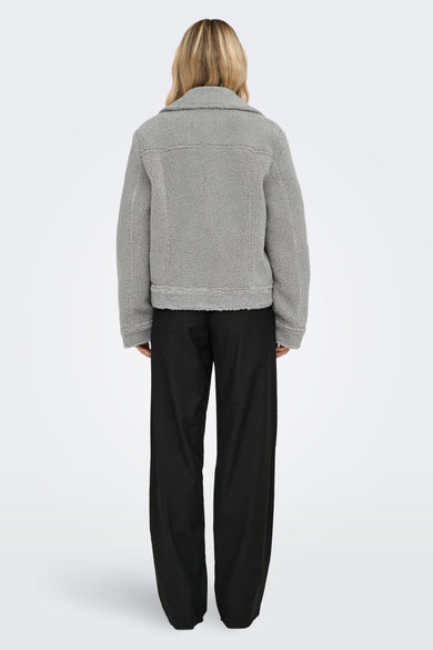 Manteau court gris d'ONLY, avec texture en fourrure de teddy, porté avec un pantalon noir, dos.