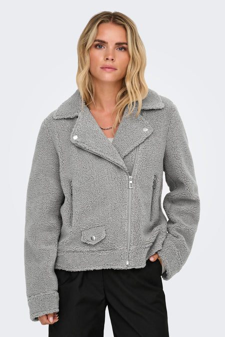 Manteau court gris d'ONLY, avec texture en fourrure de teddy et fermeture éclair argentée, porté avec un pantalon noir.
