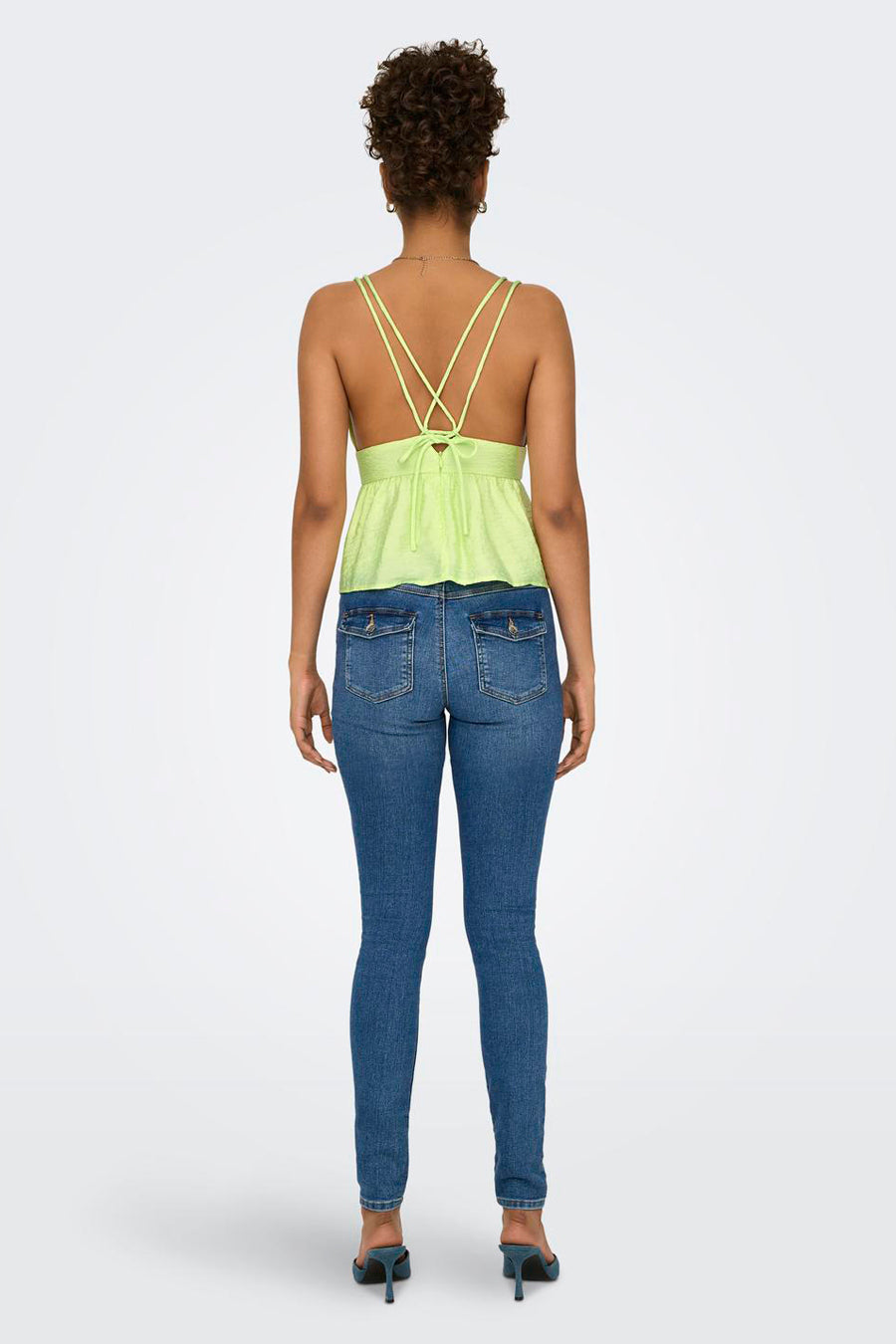 Groene mouwloze blouse van ONLY, met gekruiste bandjes en een getailleerde pasvorm, gedragen met jeans en hakken.
