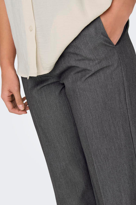 Pantalon gris d'ONLY, avec une main dans la poche et associé à une blouse claire beige.