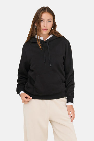 Zwarte sweater met kap van ONLY, gestyled met een witte blouse en crèmekleurige joggingbroek.
