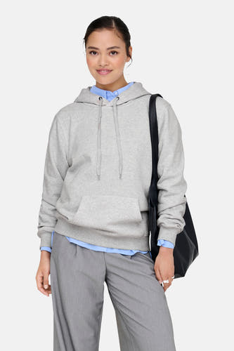 Grijze sweater met kap van ONLY®, met trekkoord en buidelzak, gedragen over een blauw overhemd en grijze pantalon.
