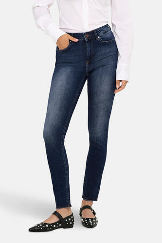Skinny jeans van donkerblauw denim van ONLY, met een witte blouse en zwarte schoenen met studs.
