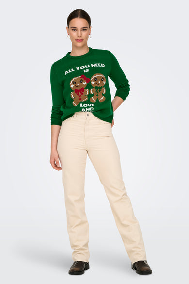 Groene trui met ronde hals van ONLY, met kerstafbeelding van peperkoekpoppen en beige pantalon en zwarte schoenen.
