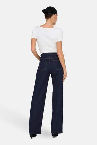 Jean bleu marine, large de ONLY, vu de l'rièrerière avec une avec blanche et des boucles d'oreilles en argent.