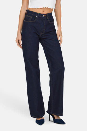 Jean bleu foncé, large de ONLY, avec des surpiqures jaunes et porté avec un haut blanc et des chaussures bleues.