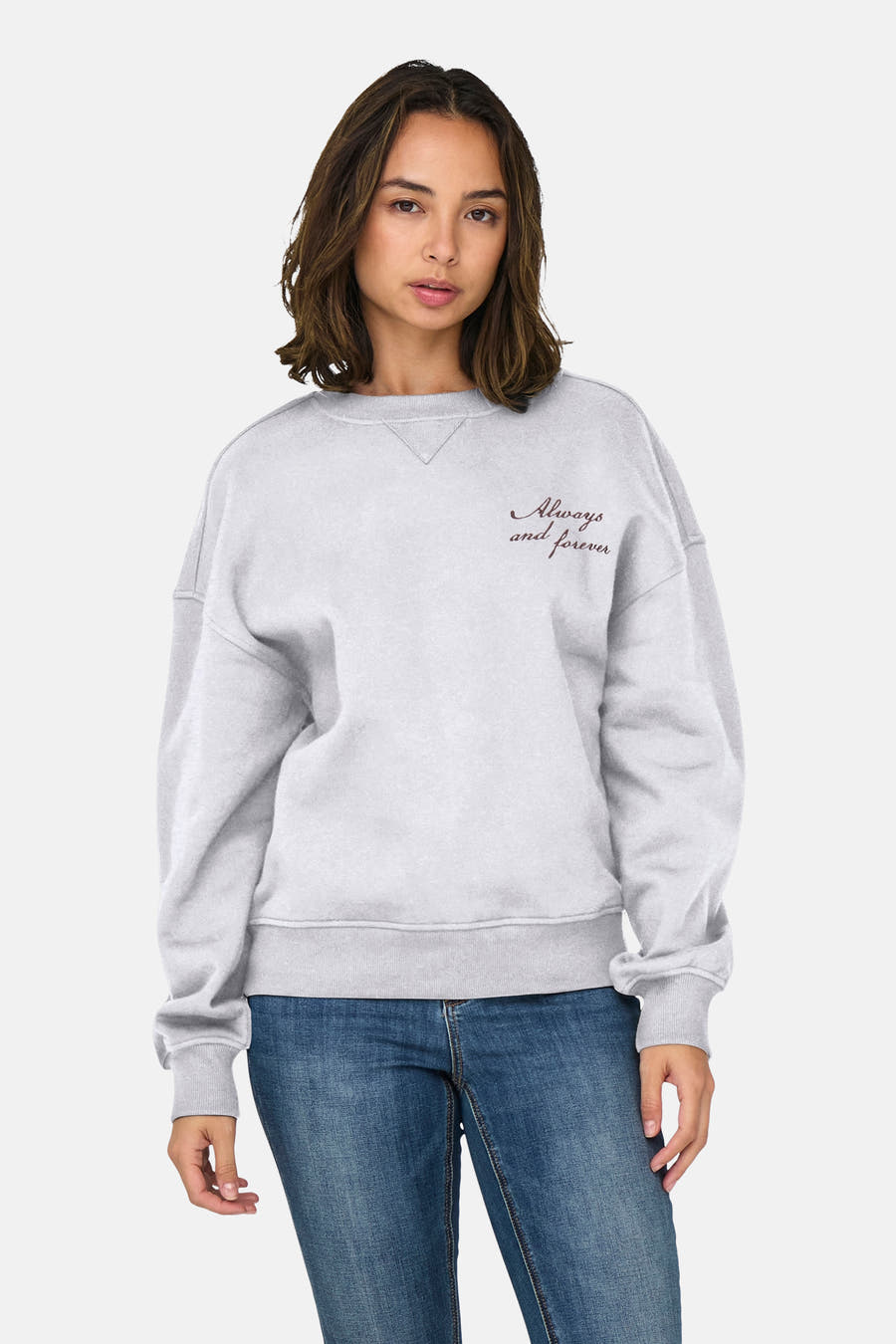 Grijze sweater van ONLY®, met ronde hals en de tekst "Always and forever" geborduurd, gedragen met een spijkerbroek.
