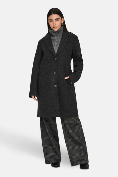 Manteau long noir de JDY, porté avec un pull gris et un pantalon rayé.