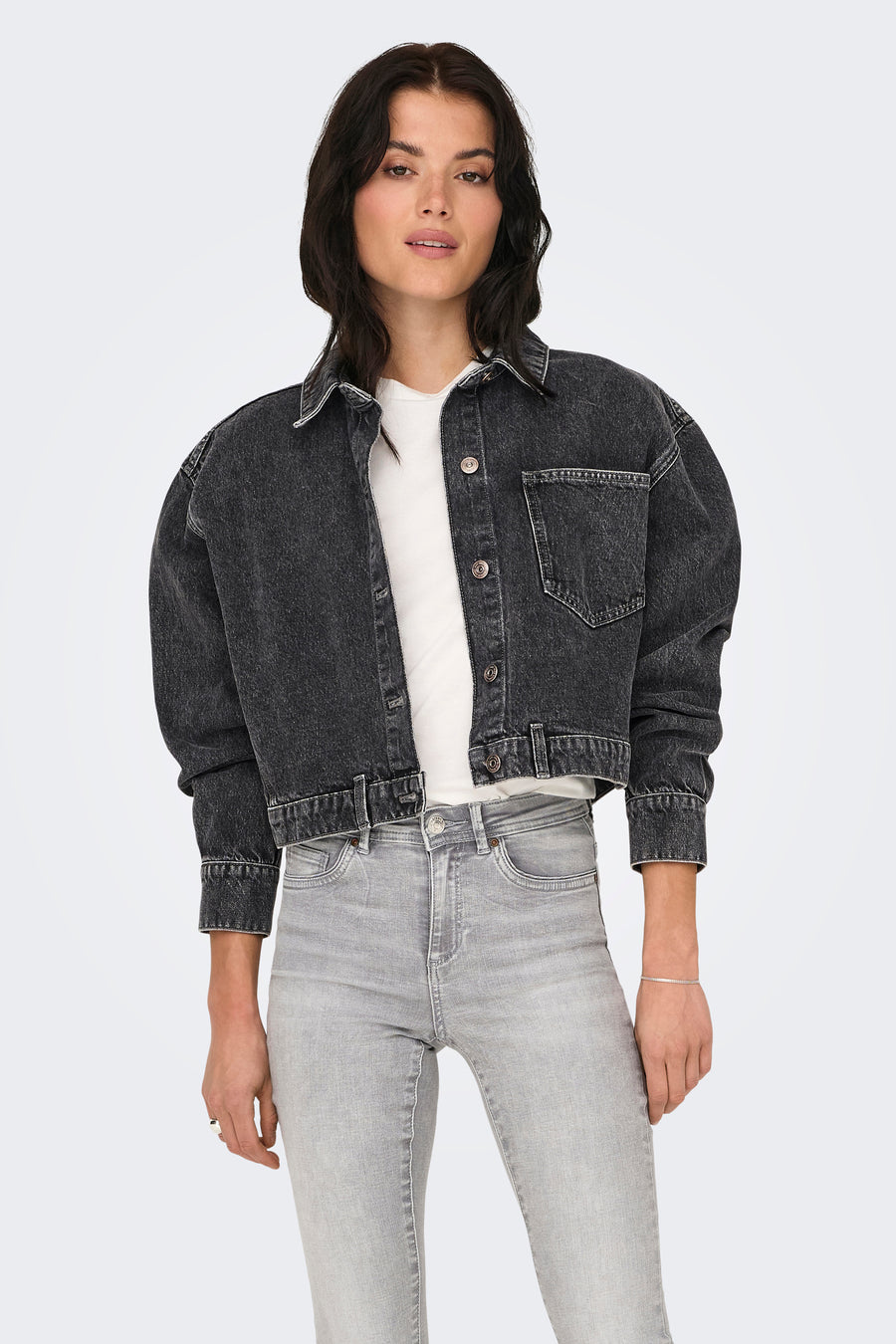 Donkergrijze jeansjas van ONLY, met knoopsluiting en een borstzak, gedragen over een wit T-shirt met grijze jeans.
