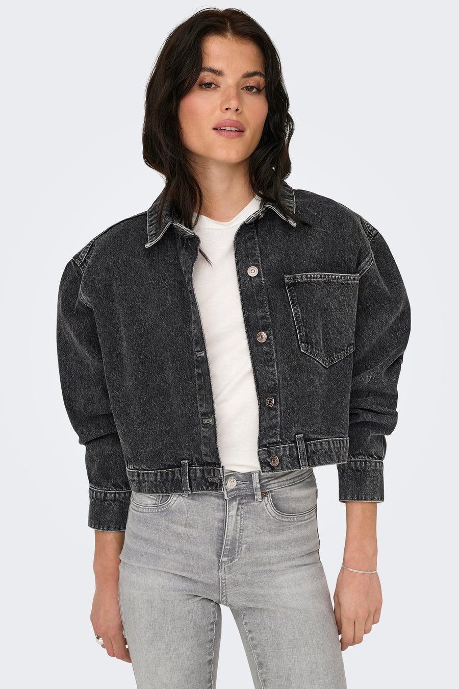 Donkergrijze jeansjas van ONLY, gedragen over een wit shirt en gecombineerd met een grijze jeans.