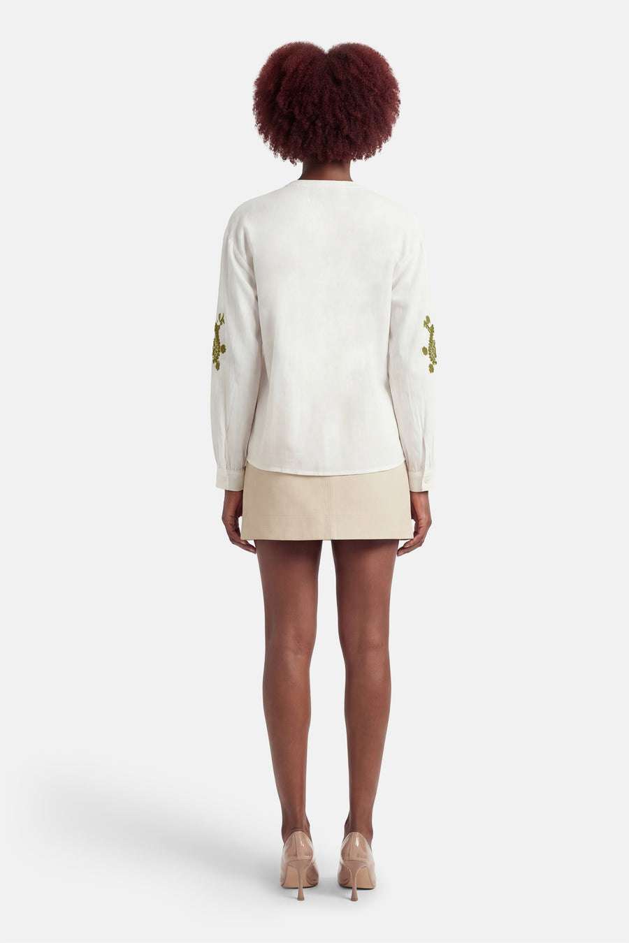Chemisier blanc à manches longues de ONLY, avec broderies vertes sur les manches, combiné avec une jupe beige et des escarpins en cuir verni.