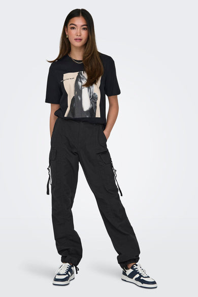 Jean cargo gris de ONLY®, porté avec un T-shirt noir imprimé et des baskets bleu-blanc.