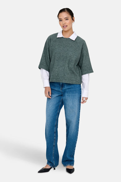 Groene trui met ronde hals van ONLY, gedragen over een wit overhemd en gecombineerd met blauwe jeans en zwarte schoenen.
