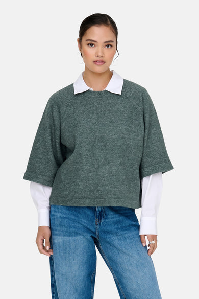 Groene trui met ronde hals van ONLY, gedragen over een wit overhemd en een blauwe spijkerbroek.
