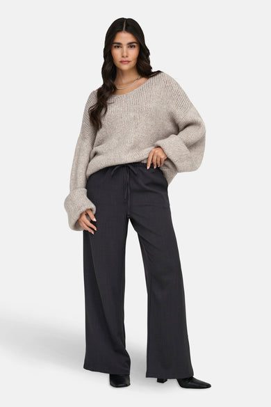 T-shirt écru avec col V de JDY, porté avec un pantalon large anthracite et une chaîne d'argent.