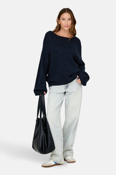Pull à col V bleu marine de JDY, avec des manches longues et associé à un jeans large et une sac noir.