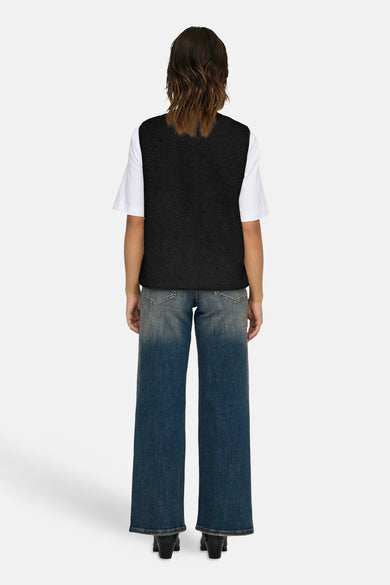Zwarte bodywarmer van ONLY, gedragen over een wit shirt met wijde blauwe jeans en zwarte laarsjes.