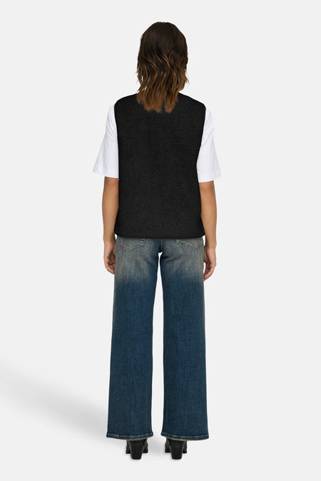Zwarte bodywarmer van ONLY, gedragen over een wit shirt met wijde blauwe jeans en zwarte laarsjes.