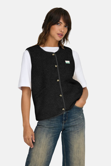 Zwarte bodywarmer van ONLY, met knoopsluiting en een label op de borst, gedragen over een wit T-shirt met jeans.

