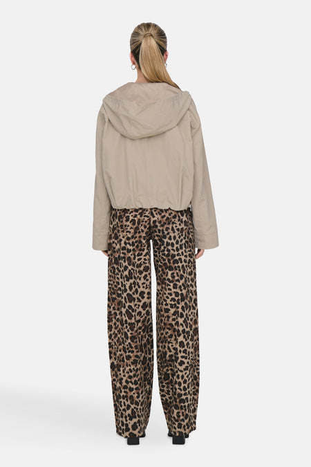 Beige korte jas van ONLY, met lange mouwen en een capuchon, gecombineerd met een broek met luipaardprint.
