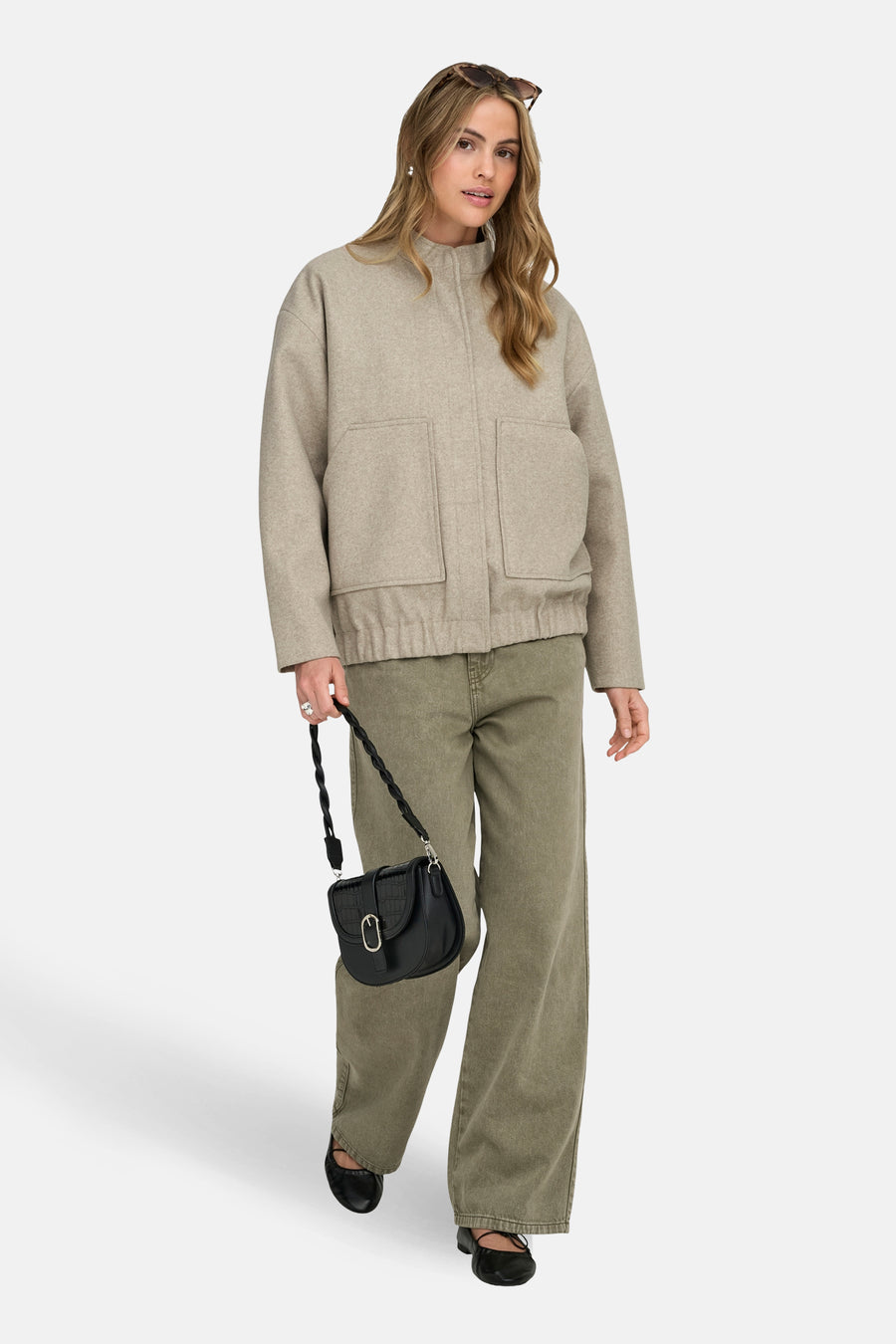 Beige korte jas van ONLY, met opgestikte zakken, gedragen met groene broek en zwarte handtas.