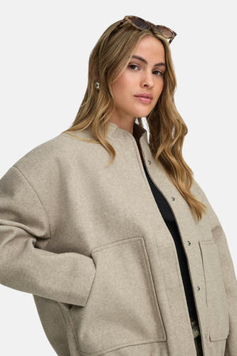 Manteau court beige de ONLY, avec des poches et des boutons-pression, porté sur une chemise noire.