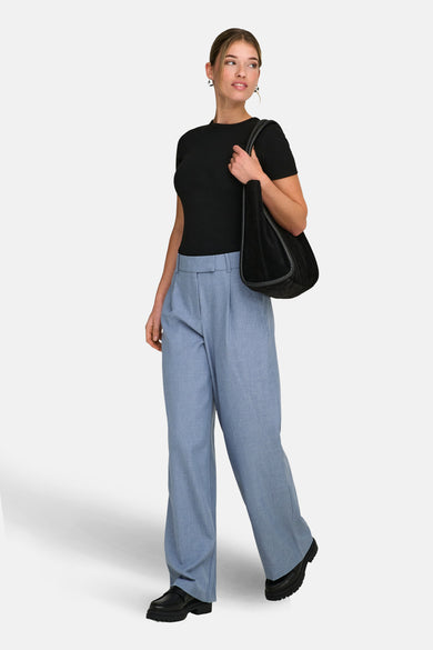 Blauwe kostuumbroek van ONLY, met wijde pijpen en gedragen met een zwart T-shirt en leren tas.
