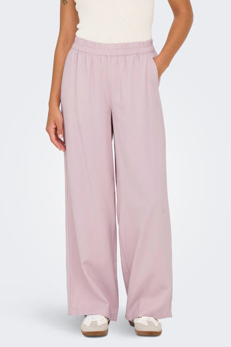 Roze broek van ONLY® met elastische tailleband, wijde pijpen en zakken, gedragen met een crèmekleurig hemd.
