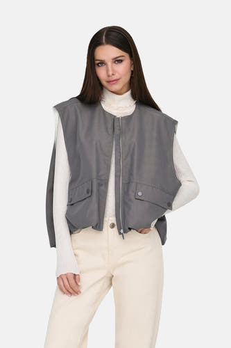 Grijze bodywarmer van ONLY, met zakken, gedragen over een witte coltrui en beige broek.
