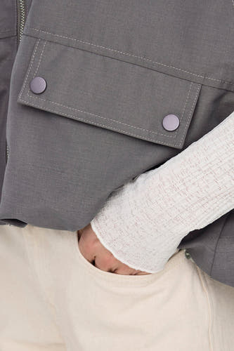 Grijs bodywarmer van ONLY, met klepzakken en een witte, gebreide mouw, in een close-up shot.
