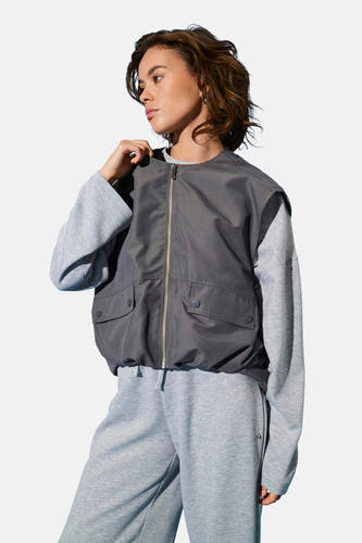 Grijze bodywarmer van ONLY, met zilverkleurige ritssluiting en opgestikte zakken, gedragen over een grijze trui en joggingbroek.