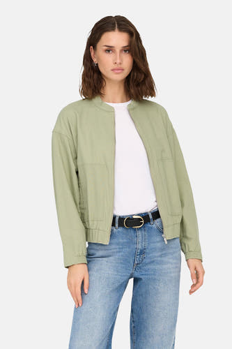 Groene korte jas van ONLY, met een ritssluiting en gedragen over een wit shirt en blauwe jeans.
