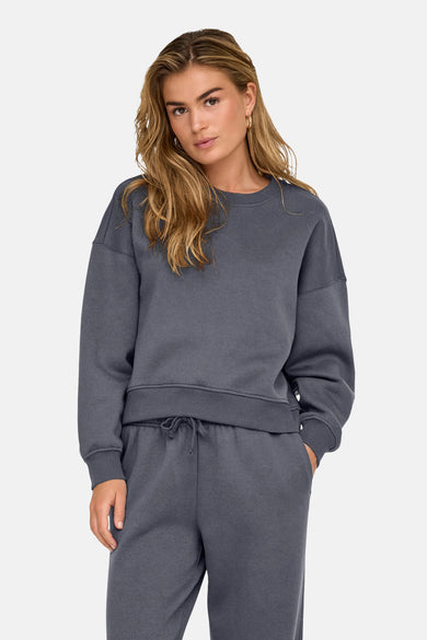 Pull-over bleu d'ONLY, avec des manches longues et porté avec un short de jogging.