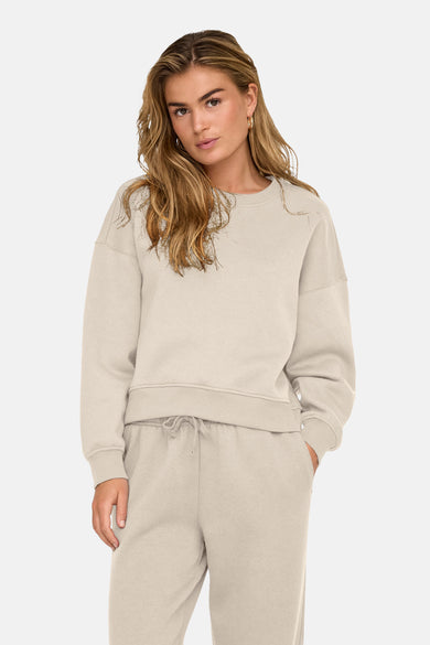 Gilet écru de ONLY, avec des manches longues, porté avec un pantalon de jogging coordonné.