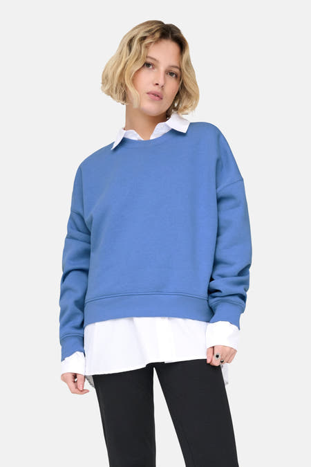 Blauwe sweater van ONLY®, met een witte blouse eronder en een zwarte broek.