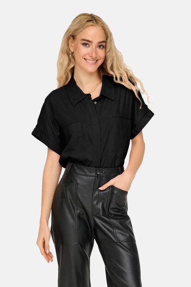 Chemise noire à manches courtes de ONLY, portée avec un pantalon en cuir et des bijoux en or.