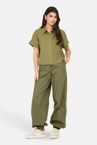 Kaki hemd met korte mouwen van ONLY, gedragen met groene broek en crèmekleurige sneakers.
