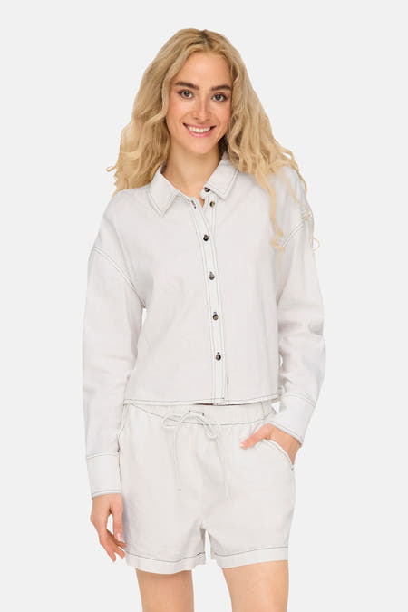 Chemise blanche à manches longues de ONLY®, avec des ourlets sombres et portée avec un short coordonné.