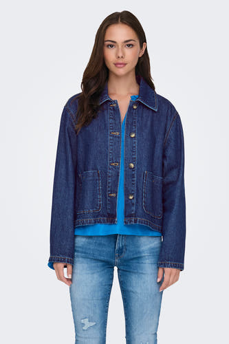 Donkerblauwe jeansjas van ONLY, gedragen over een blauwe top en gecombineerd met een lichte jeans met scheuren.
