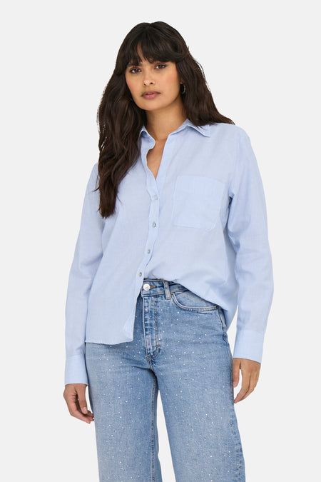 Chemise bleue ONLY, à manches longues et avec une poche poitrine, combinée avec un jean ample et des talons.